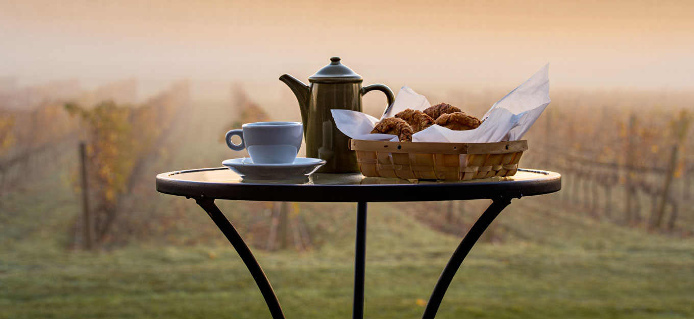 Morning coffee and fresh pastries on a table in Napa Valley as fog lifts over the valley floor during early light.