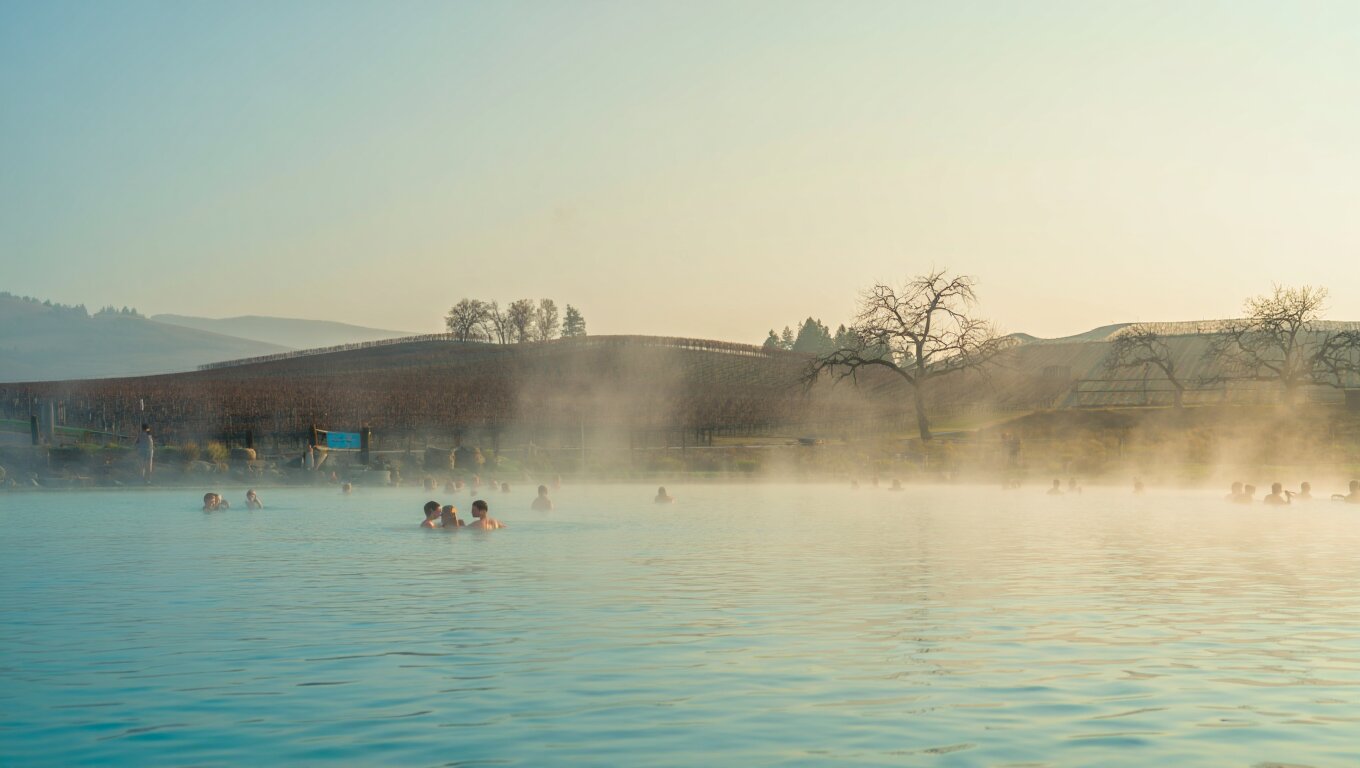 Steam rising from a natural mineral pool in Calistoga, Napa Valley, with surrounding hills and early morning light.
