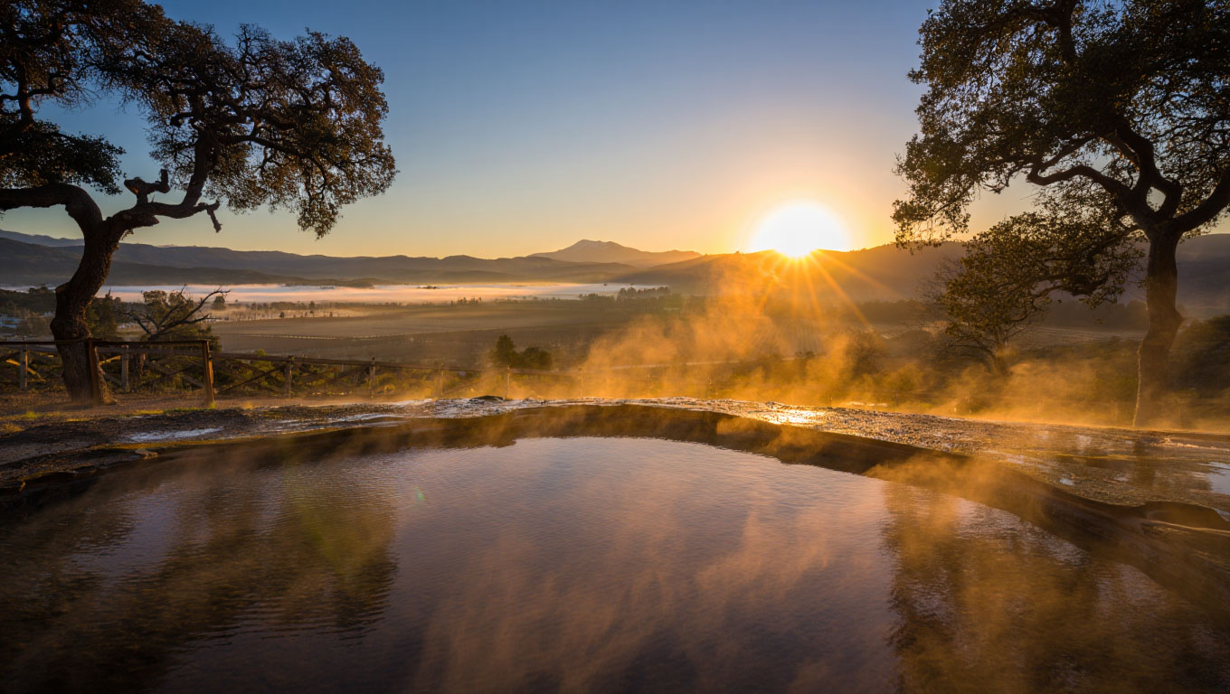 Early morning geothermal mineral pool in Calistoga with steam rising and oak trees in soft fog.