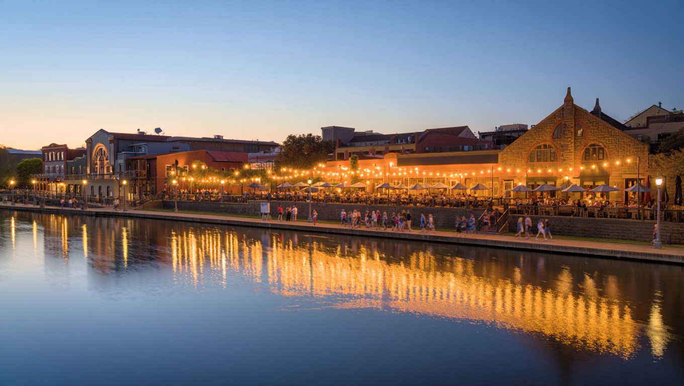 Early evening view of downtown Napa along the riverfront with people walking and restaurant lights reflecting on the water.