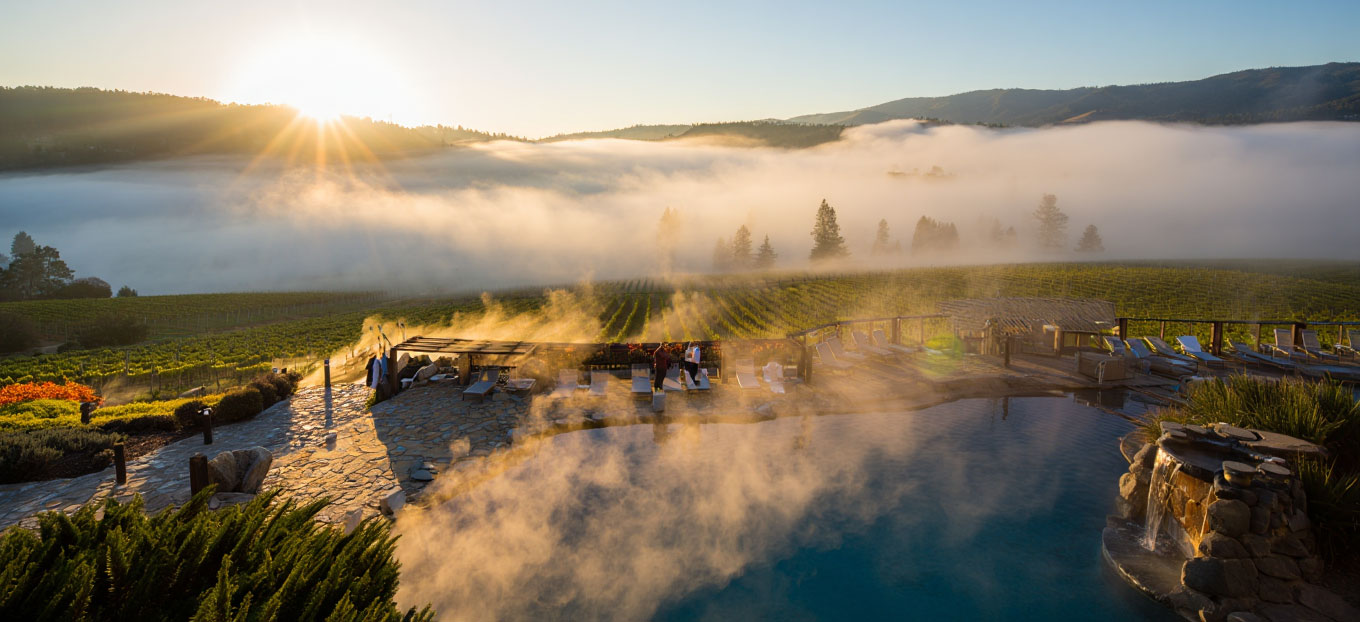 Early morning view of a Calistoga spa resort with a steaming geothermal mineral pool and fog drifting across Napa Valley hills.