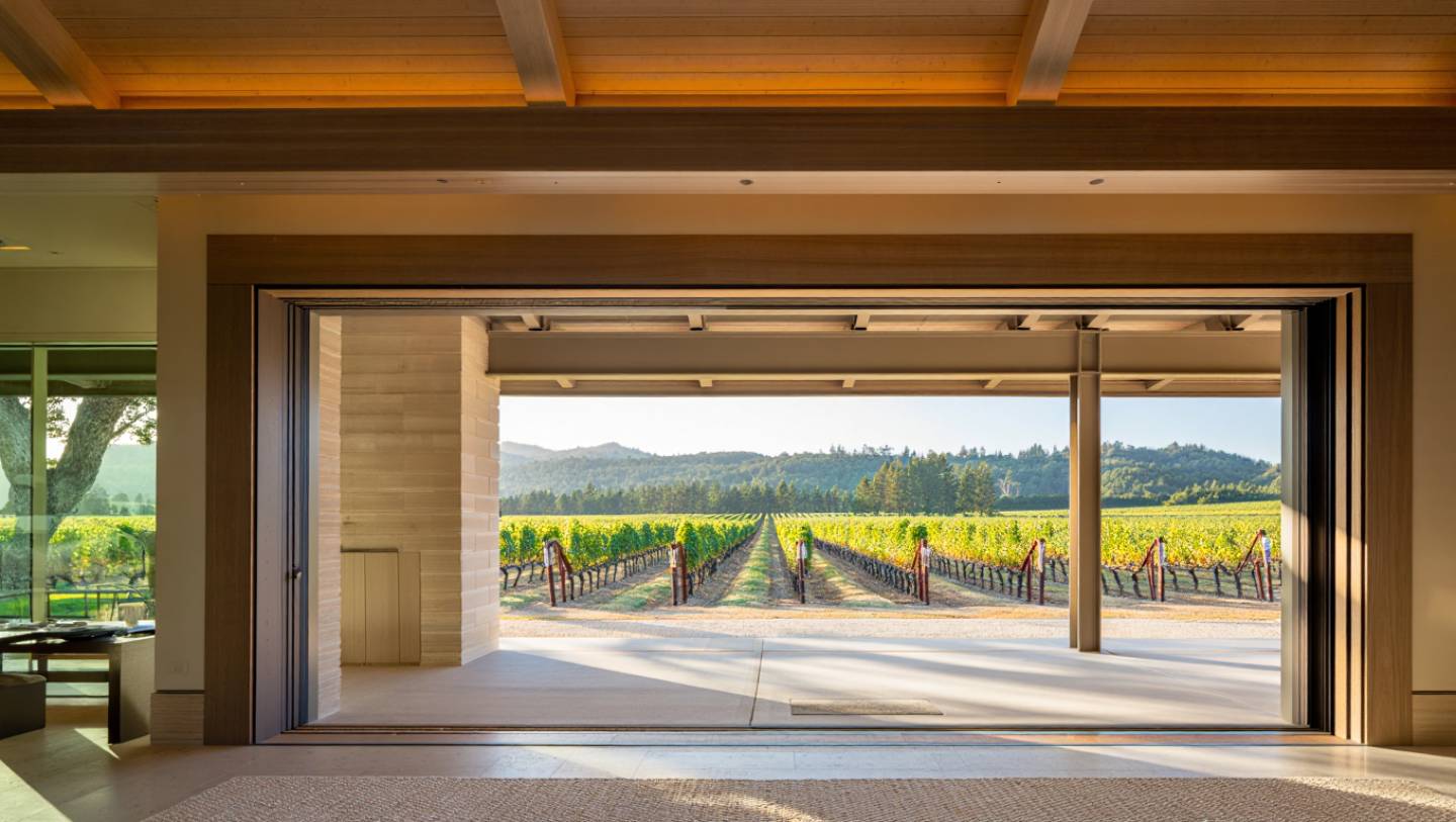 Indoor outdoor architectural space in Napa Valley with concrete floors, wood beams, and open views to vineyards.