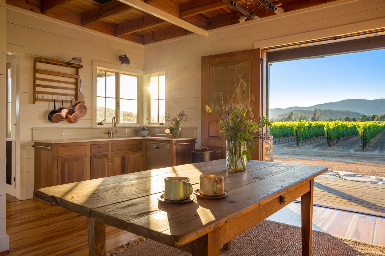 Morning light inside a Napa Valley vacation rental kitchen with coffee cups on a wooden table and an open door to the outdoors.
