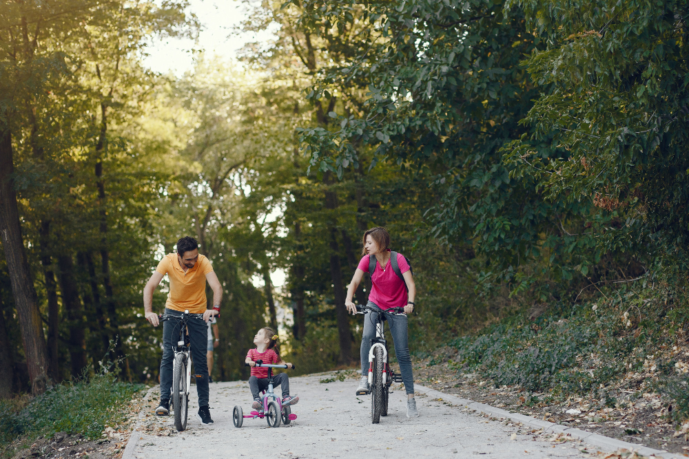 A family riding bicycles on the Napa Valley Vine Trail with vineyard rows and the Napa River beside them during a calm morning.