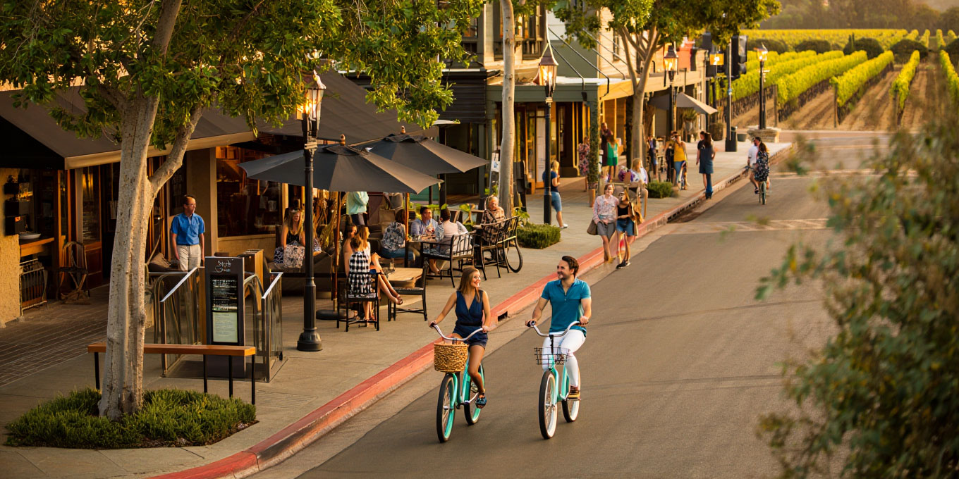 Guests walking and biking through Yountville in the afternoon with vineyards visible beyond the town.