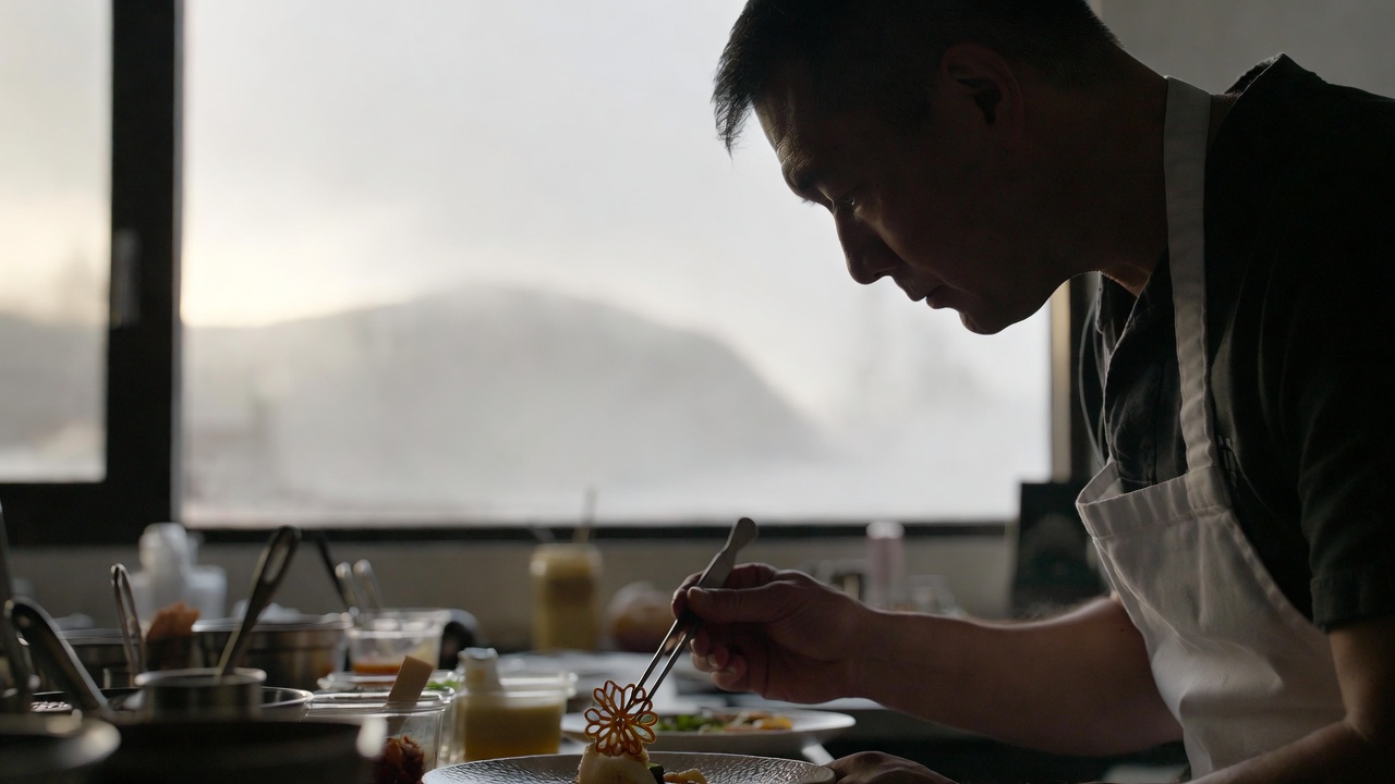 A chef in a white coat carefully plating a seasonal dish in a Napa Valley kitchen, lit by soft, diffused morning light coming through a large window.