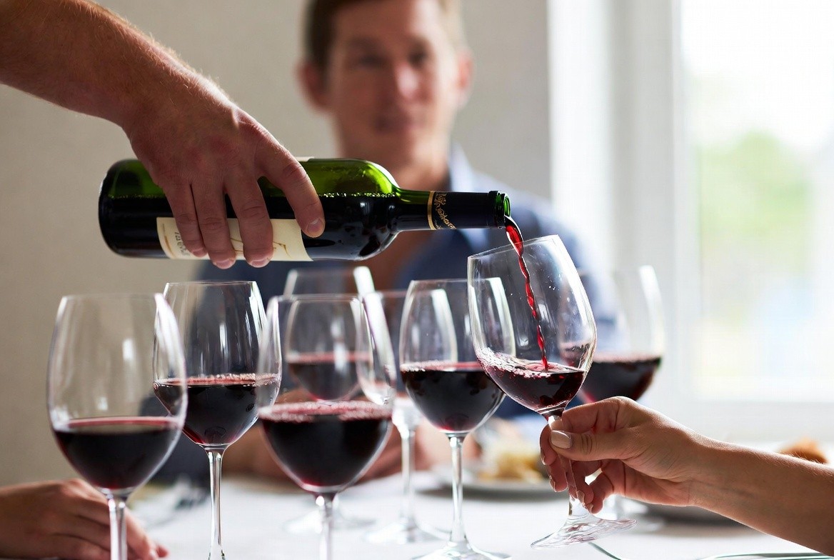 Host pouring wine into a glass at a dinner table, showing relaxed Napa Valley–inspired hospitality and thoughtful hosting at home.