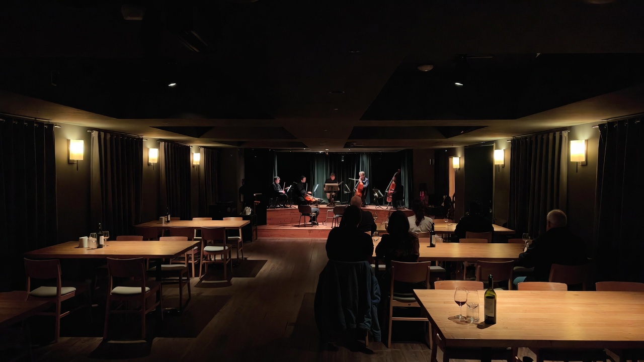 Seated guests listen quietly to an acoustic music performance in a small Napa Valley venue at dusk, with warm lighting, wood textures, and an intimate, calm atmosphere designed for focused sound.
