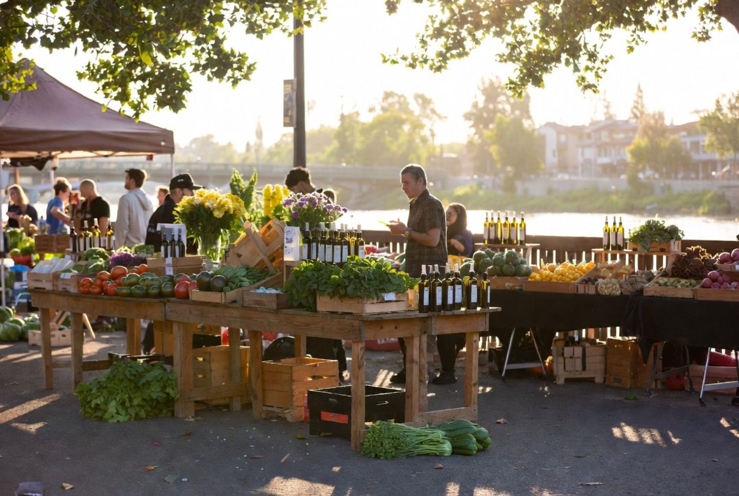 Farmers market in downtown Napa Valley during early morning with heirloom tomatoes, leafy greens, flowers, and local olive oil displayed on wooden tables near the Napa River.