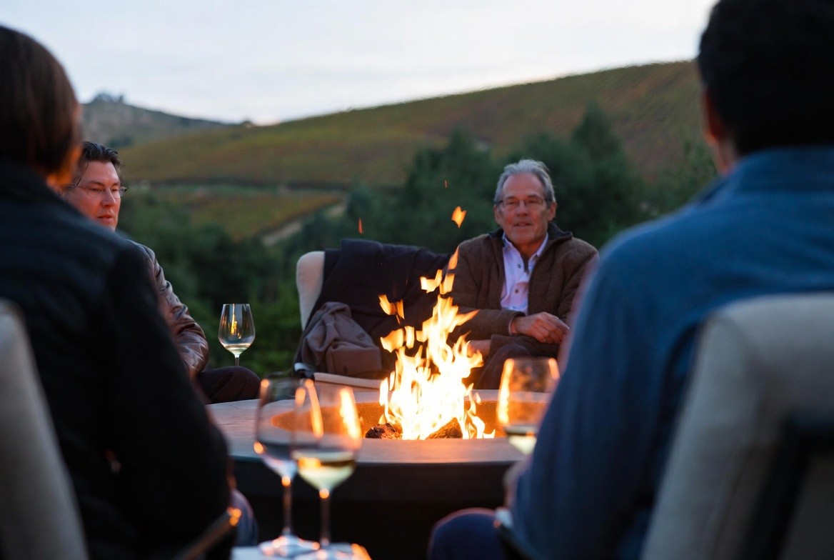 Friends sitting together around a fire pit in Napa Valley during a cool autumn evening, enjoying wine and conversation during a Friendsgiving weekend.