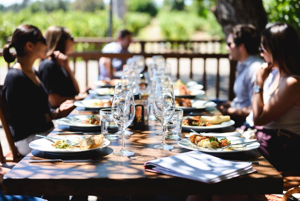 Relaxed long lunch at a Napa Valley restaurant patio with wine glasses and a notebook, illustrating slow travel, writing, and personal documentation.
