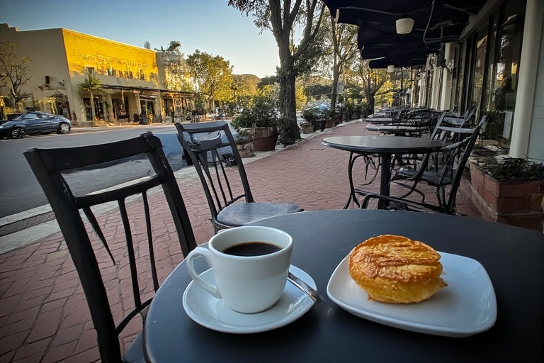 Pastry and coffee on a sidewalk table in a Napa Valley town during a quiet early morning before shops and wineries open.
