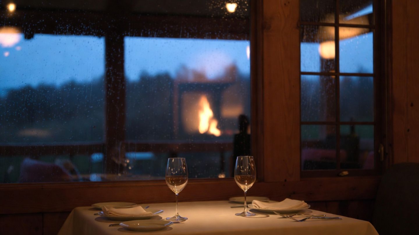 Warm restaurant interior in Napa Valley with soft lighting and rain visible through windows, representing a comfortable rainy day dining experience.