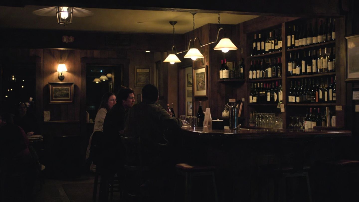 Cozy Napa Valley wine bar interior at night with patrons seated at the bar and shelves of wine bottles behind them.