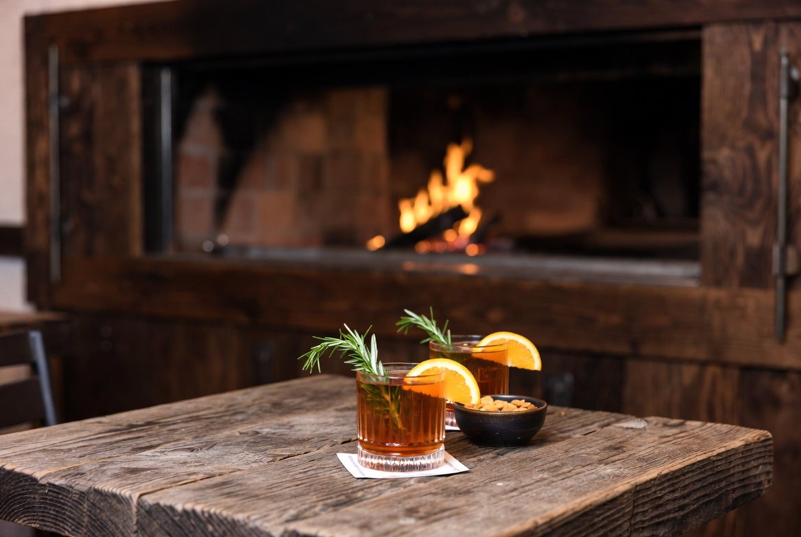 Pre dinner craft cocktails on a wooden table at The Charter Oak in St. Helena Napa Valley with wood fired kitchen glow in the background.