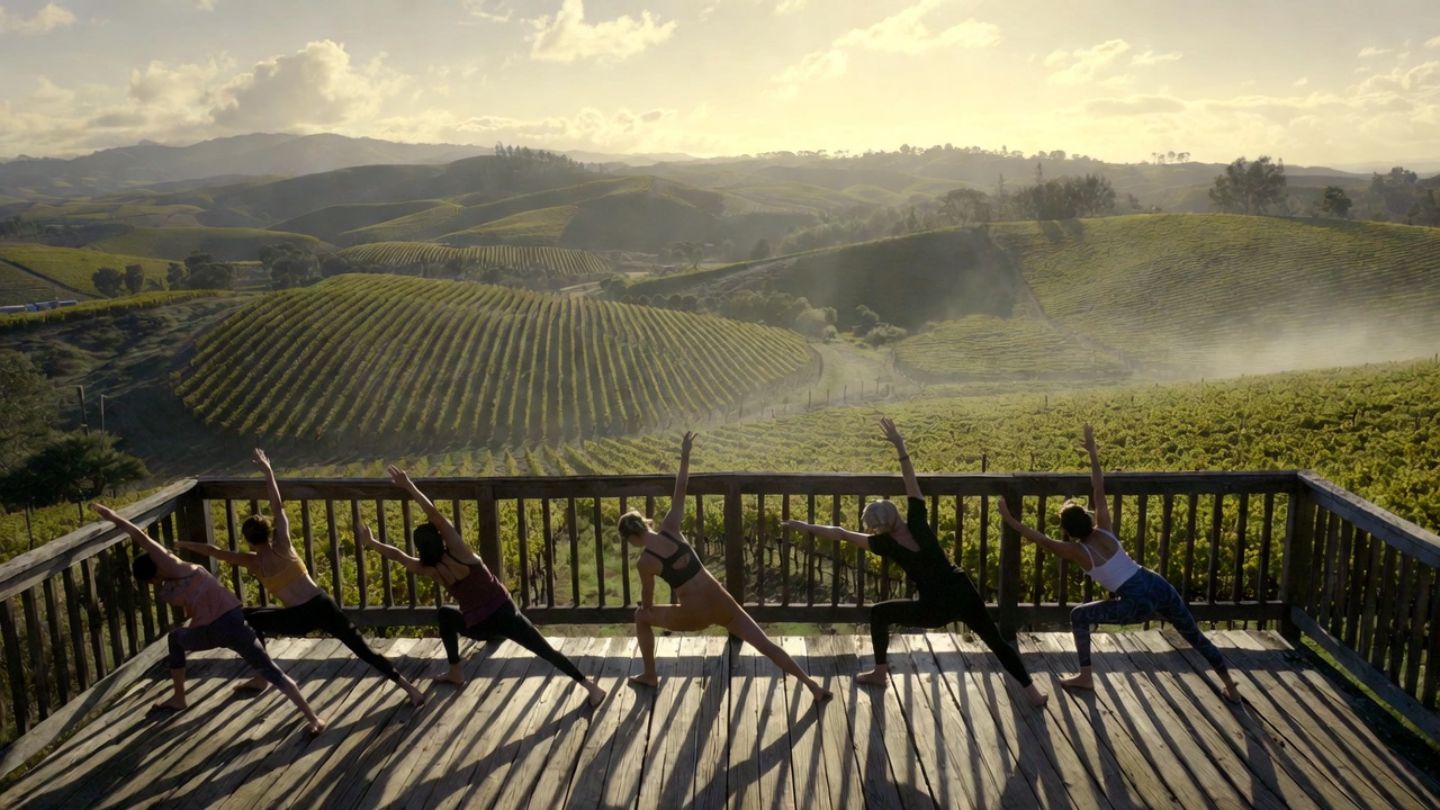 A group of people practicing yoga on an outdoor platform at a Napa Valley vineyard during a foggy sunrise.