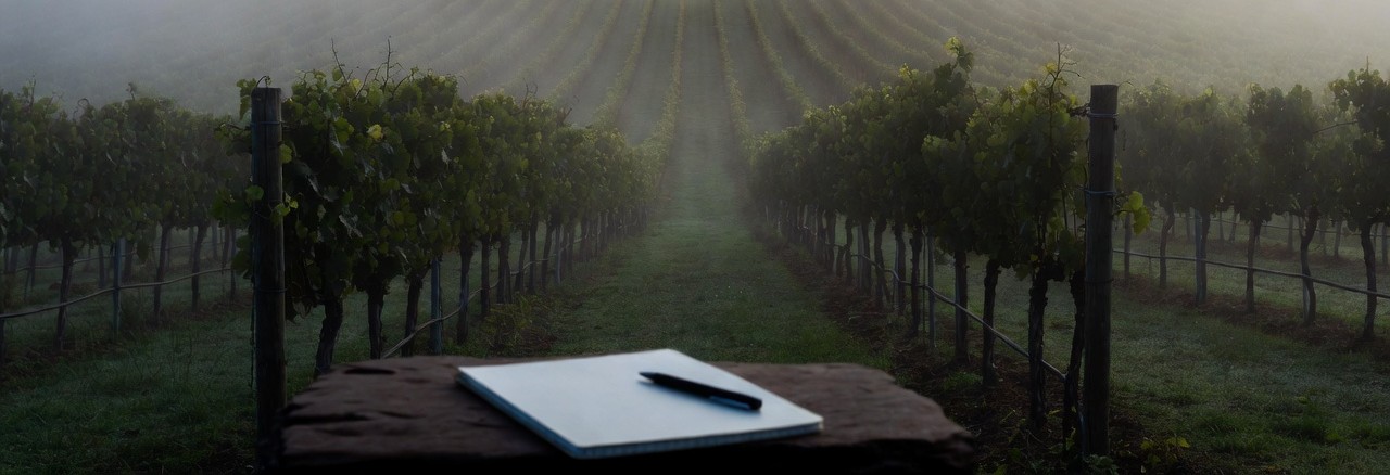 Notebook and pen on a wooden surface overlooking fog-covered vineyards in Rutherford, Napa Valley, early in the morning during a quiet writing retreat.