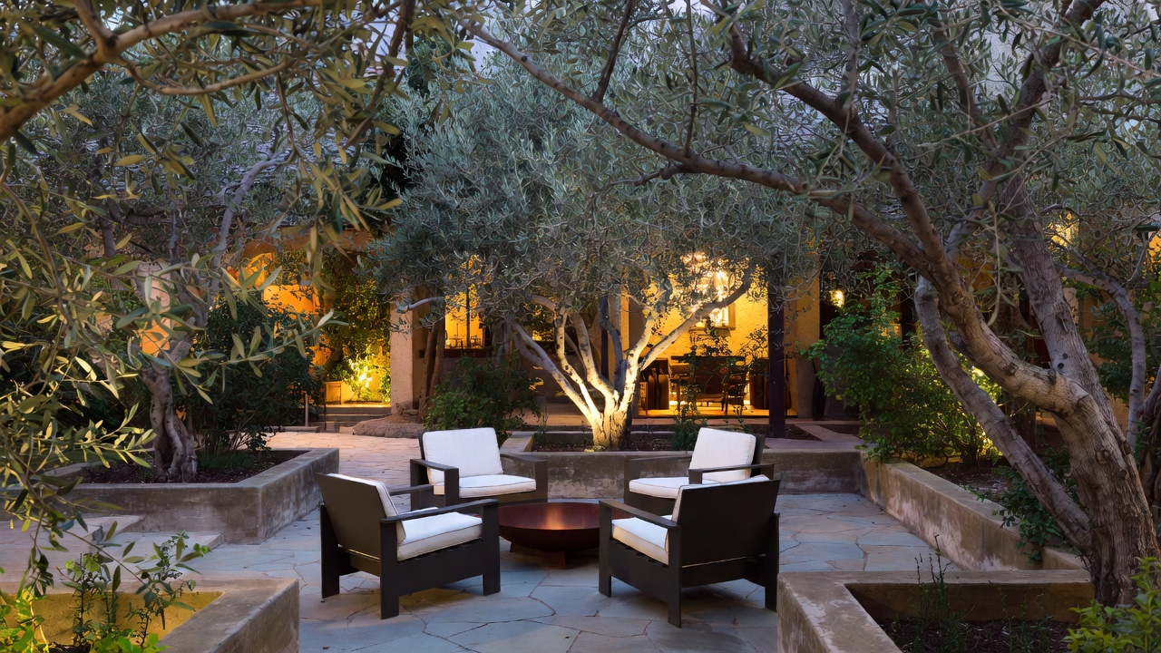 An intimate, human-scale garden courtyard in Yountville, Napa Valley, featuring a fire pit, olive trees, and stone walls, showcasing residential design for outdoor living.